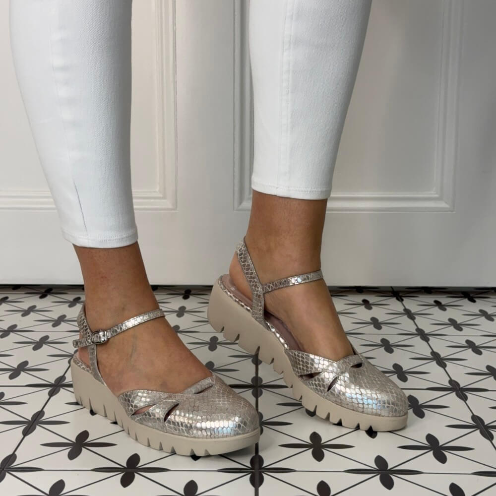 beige gold platform sandals worn with white pants on a patterned floor.