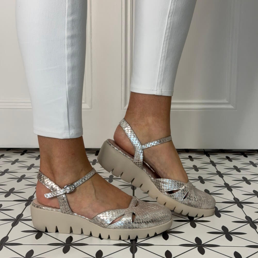 Beige Gold sandals worn with white pants on a patterned floor.