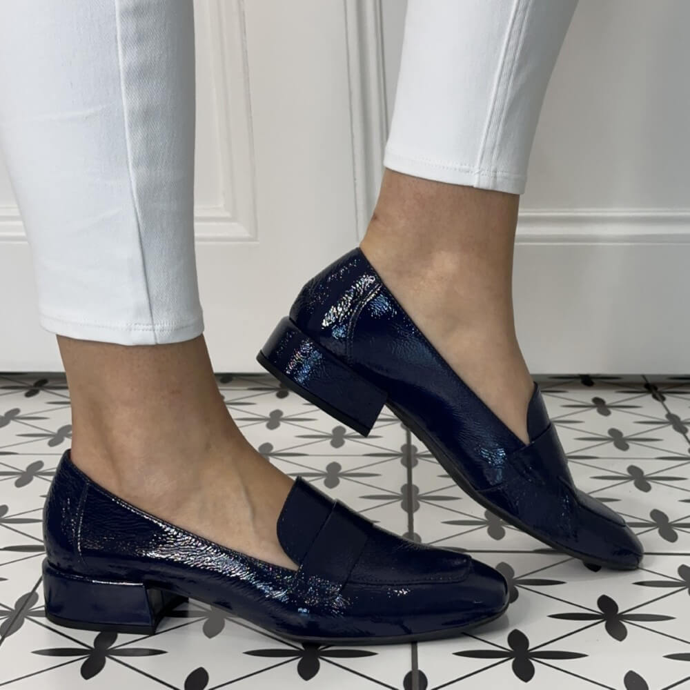 Navy blue loafers worn with white pants on a patterned floor.