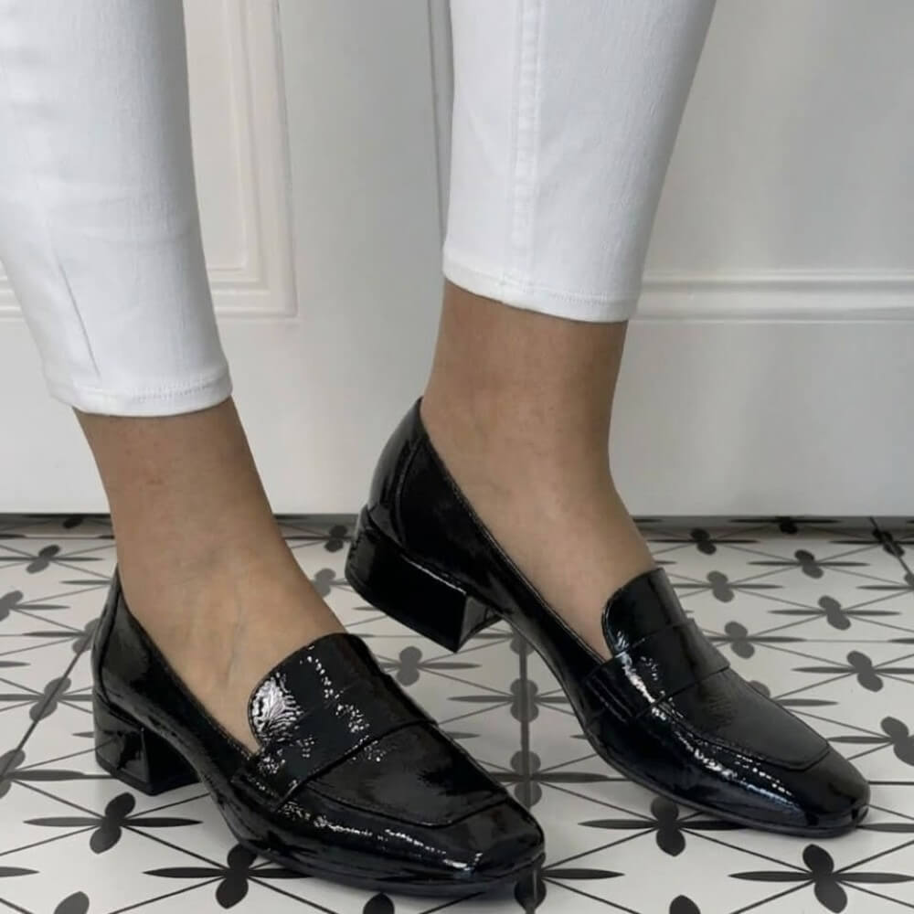 Wonders Black patent leather shoes worn with white pants on a patterned floor.