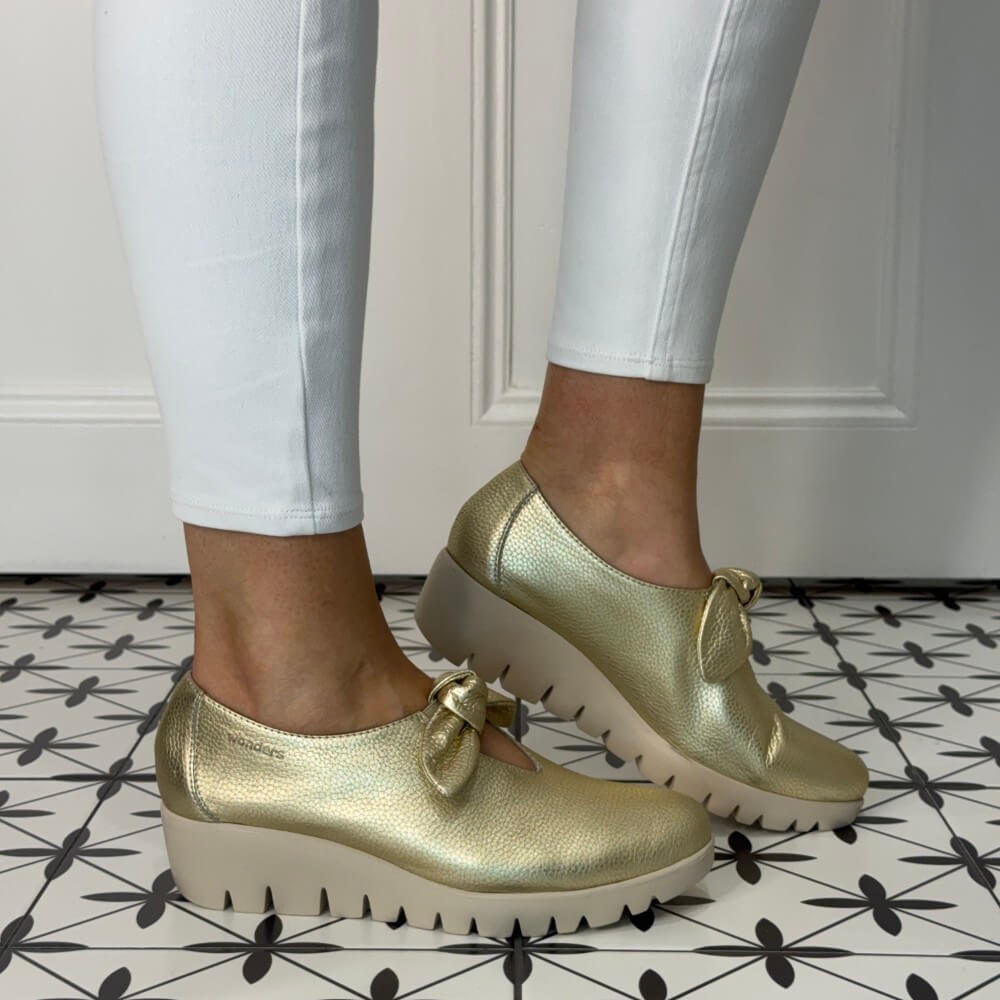 Gold platform shoes worn with white pants on a patterned floor.