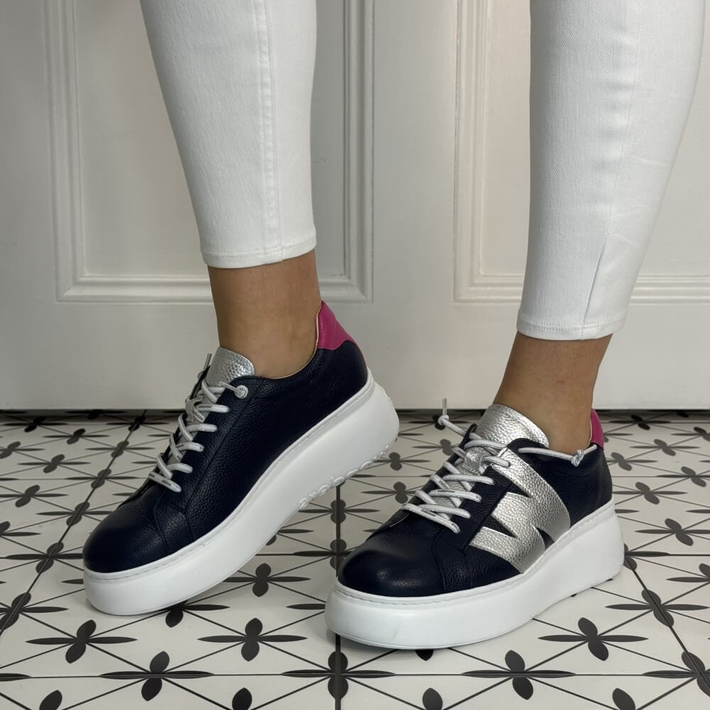 navy sneakers with white soles worn with white pants on a patterned floor.