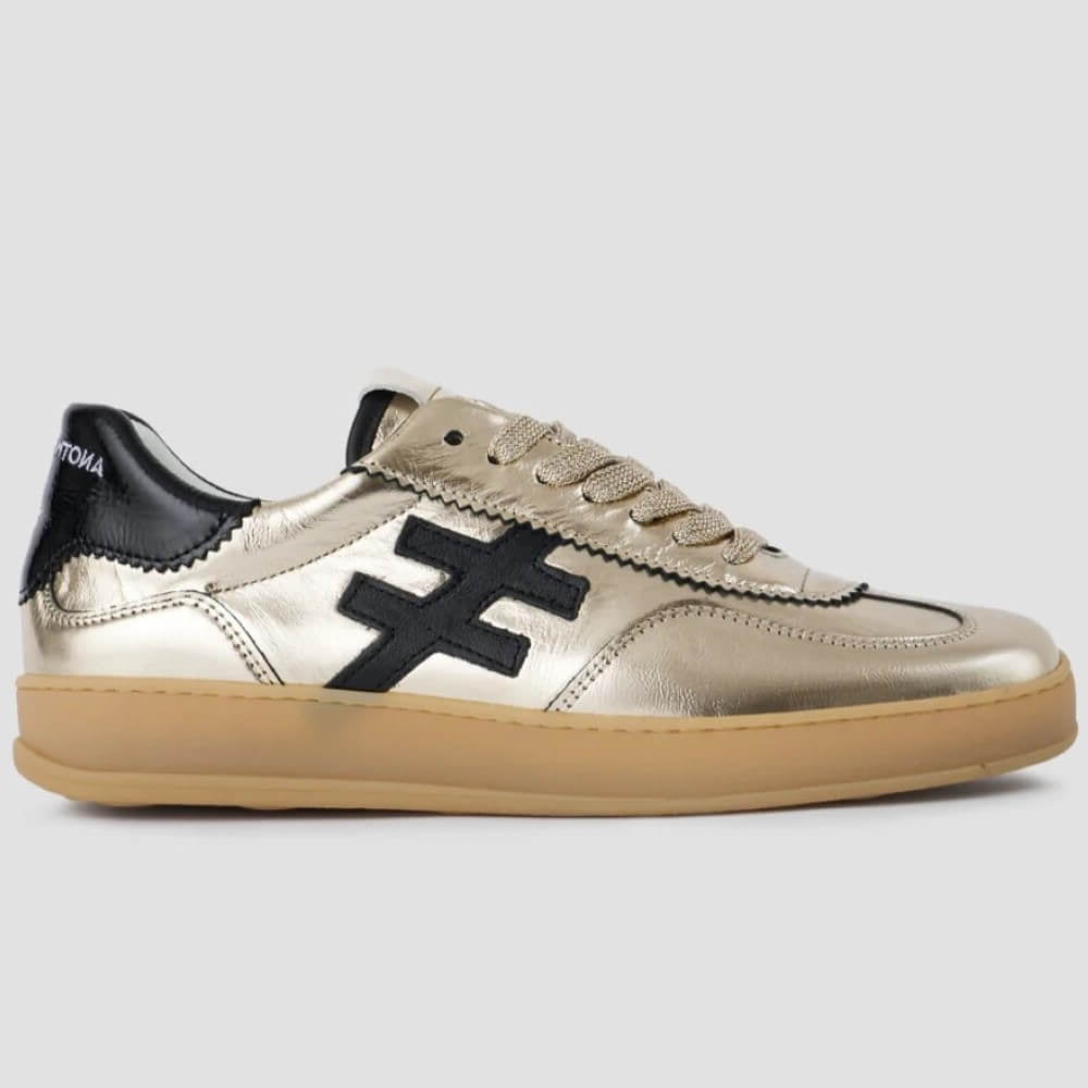 Gold leather sneaker with black logo and sole on a light grey background Another Trend