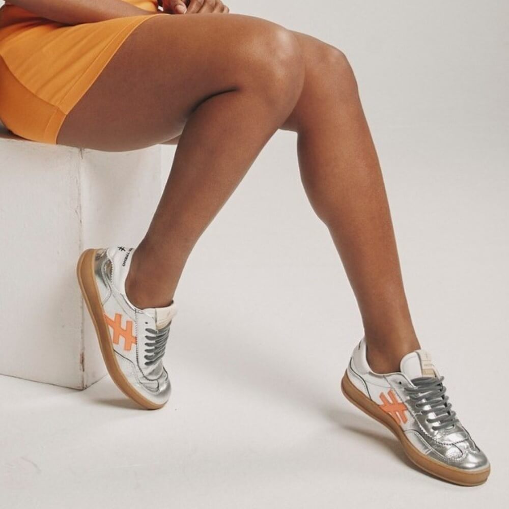 Person wearing silver sneakers with orange accents on a white background