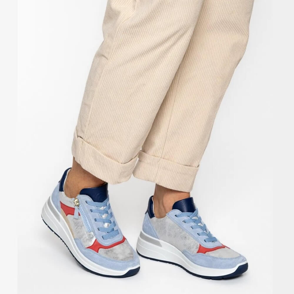 Light blue sneakers with red accents worn with beige pants on a white background