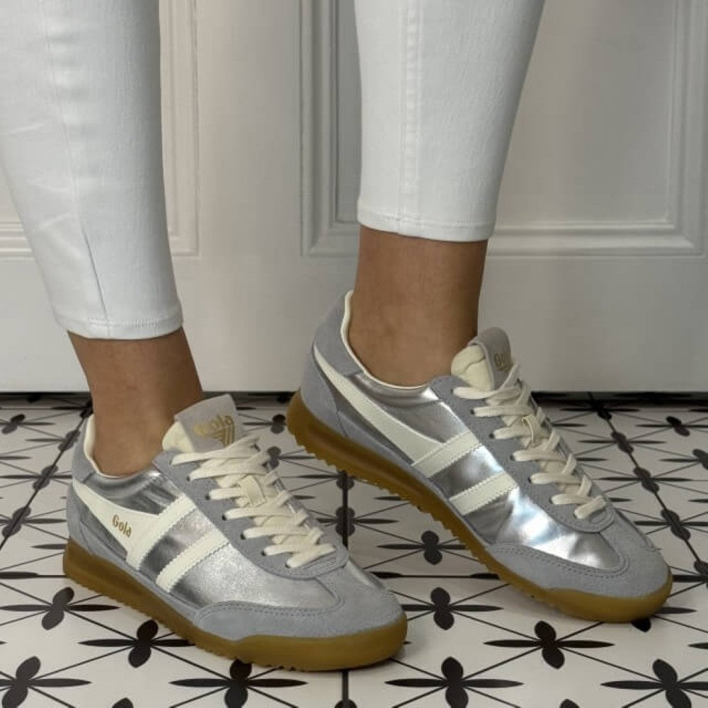 Gola Firefly Silver sneakers with brown soles worn with white pants on a patterned floor.