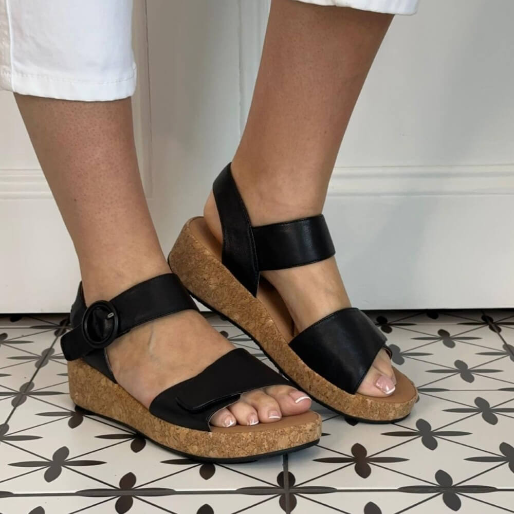 Josef Seibel Black leather sandals with cork sole worn by a person on a patterned floor.
