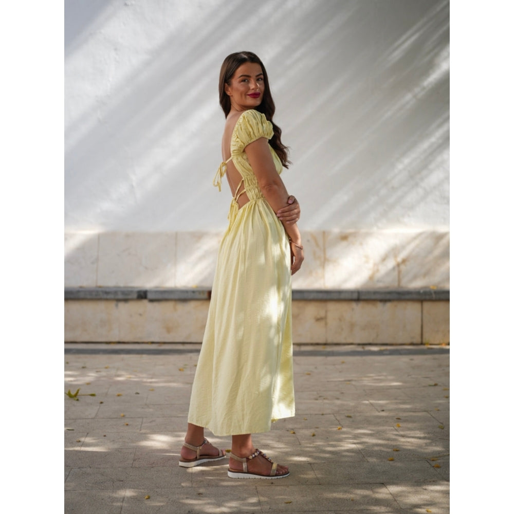 Woman wearing a yellow dress standing outdoors with a white tent-like structure in the background.